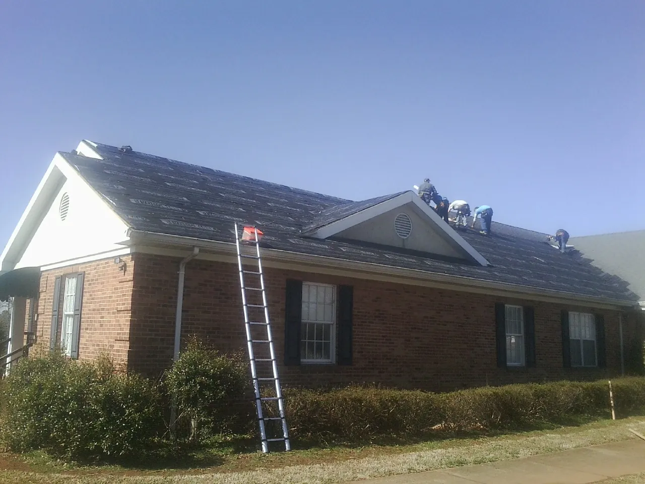 Crew tearing shingles off a brick ranch roof with a ladder set — Emergency Roof Repair work by our crew in Cornwall