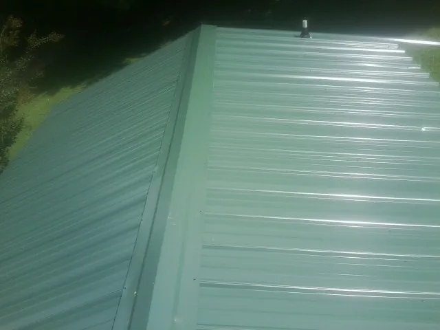 New green metal panels meeting at the ridge of a roof — Flat Roof Repair work by our crew in Cornwall