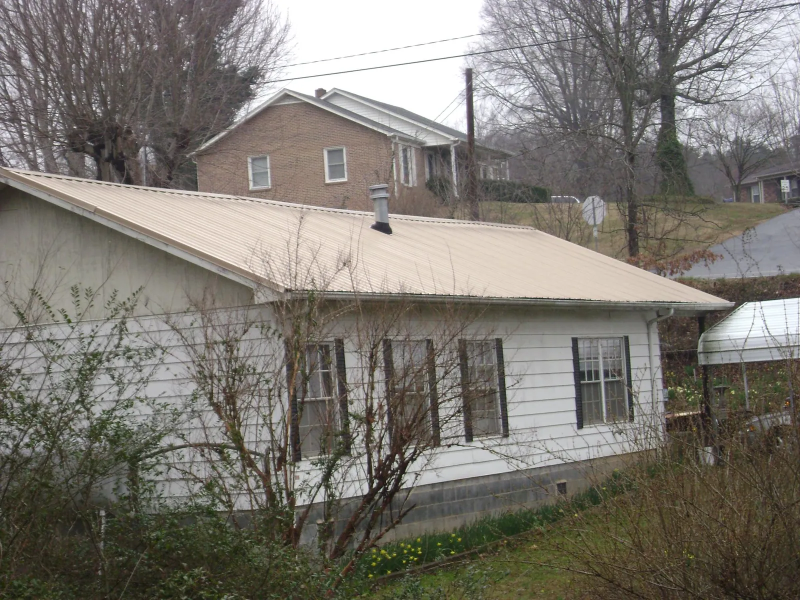 Tan metal roof on a white sided house set into a hillside — Commercial Roofing by Roofing Brothers in Cornwall